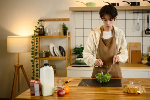 Young asian man preparing healthy vegetable salad in modern kitchen.