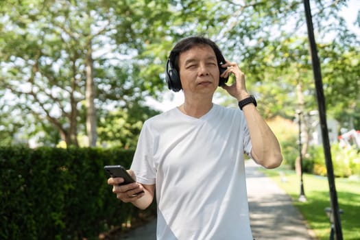 A senior man listens to music with headphones while walking in a park, promoting wellness and outdoor activity.