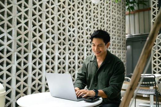 Smiling adult businessman working on his laptop at an outdoor cafe in the city.