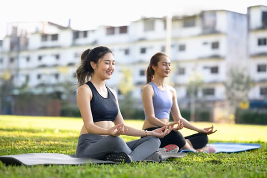 Two young women practicing yoga together in a serene outdoor park.