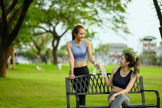 Fit women in sportswear hydrating and relaxing on bench after a workout outdoors.