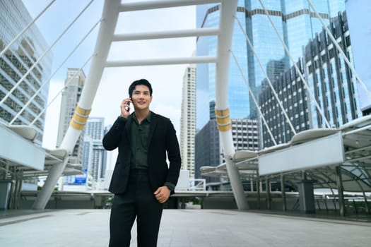 Successful businessman walking through a modern cityscape while talking on his phone.
