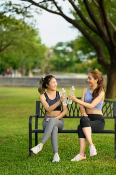 Fit women in sportswear hydrating and relaxing on bench after a workout outdoors.