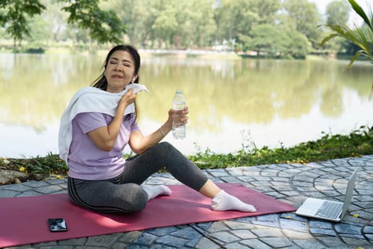 A woman wipes her sweat and drinks water after yoga, emphasizing wellness and hydration in nature.