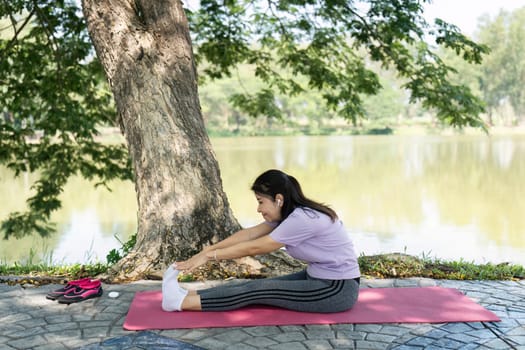 A woman engages in yoga stretches outdoors, enhancing her self-care routine in a serene lakeside environment.