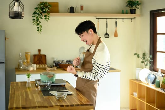 Man cook singing into spoon like microphone while preparing food in modern kitchen..