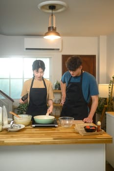 Man and woman in aprons starting to make pancakes in cozy home kitchen.