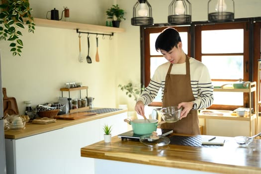 Young man cooking at home in kitchen stirring food in a pot while preparing a meal.