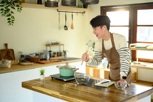 Man cook singing into spoon like microphone while preparing food in modern kitchen..