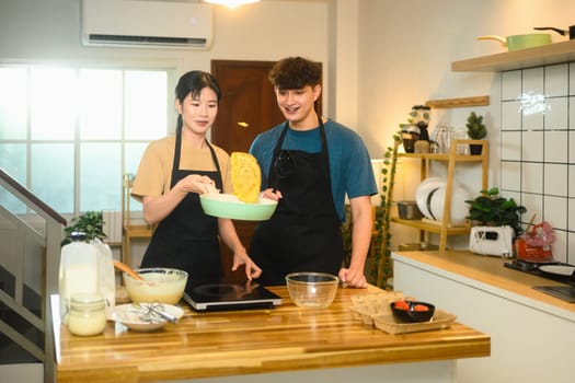Cheerful young couple enjoying time together while flipping a pancake in the kitchen.