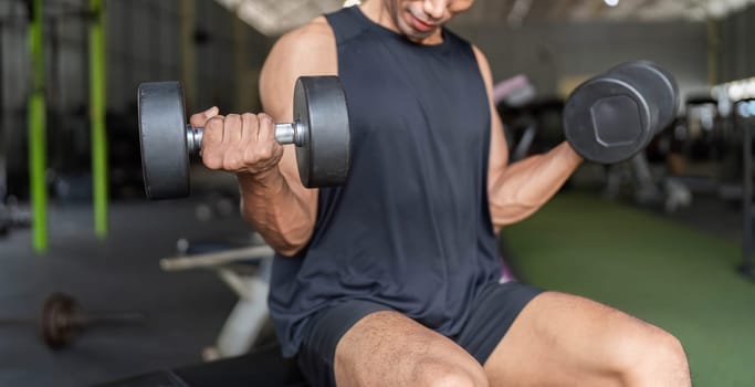 A dedicated young man engages in strength training by performing bicep curls with dumbbells in a modern gym environment.