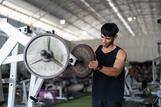 A young male athlete lifts weights with concentration in a gym setting, emphasizing fitness and strength training.