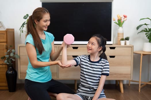 A mother assists her daughter with a pink dumbbell, promoting fitness and healthy habits in a supportive environment.