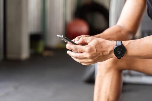 A man sits in the gym, focused on his smartphone, tracking his fitness progress and workouts using a fitness app.