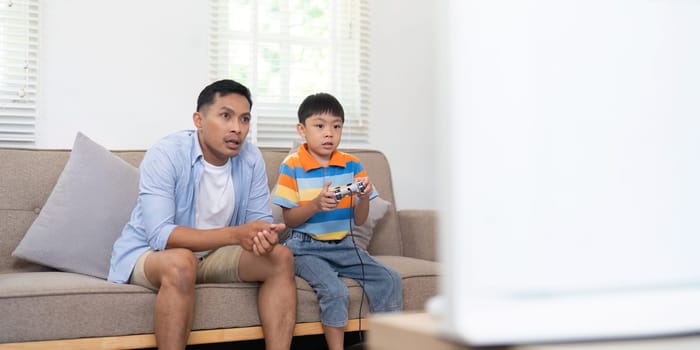 A father and son are focused on their gaming session, sitting on a couch and enjoying their time together.