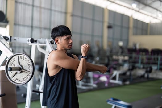A young man performs arm stretches in a gym, focusing on fitness and flexibility, preparing for an intense workout.