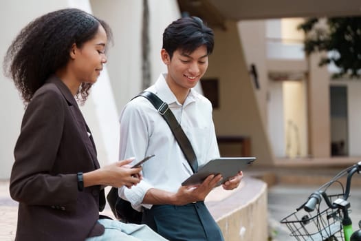 A man shows a friendly smile while discussing something on his tablet with a woman, emphasizing a blend of technology and personal connection in a sustainable environment.