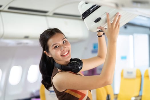 A joyful traveler on a flight, smiling while placing her bag in the overhead compartment, embodying the excitement of travel.