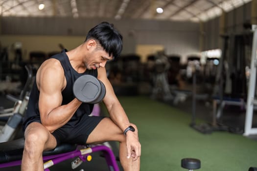 A man focuses on his form while lifting a dumbbell in a gym, highlighting his commitment to strength training.