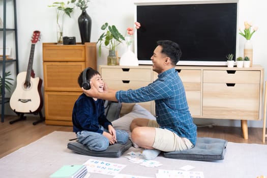 A father and son share a light-hearted moment while studying with headphones, emphasizing fun in education at home.