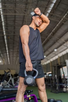 A young man showcases his strength and fitness by performing a kettlebell exercise in a gym, highlighting his workout routine.