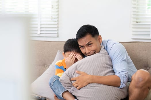 A father holds his scared son close while watching a suspenseful movie, emphasizing their protective relationship.