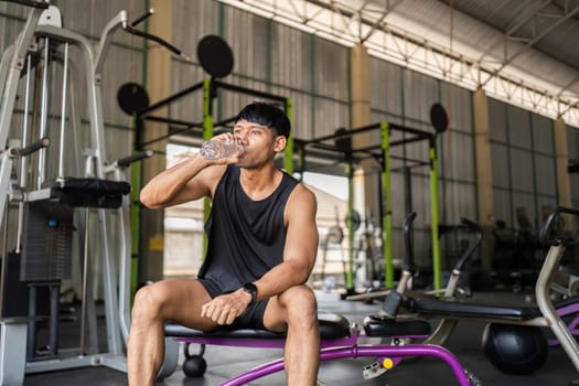 A man takes a refreshing drink of water after an intense workout session in the gym, emphasizing hydration and health.
