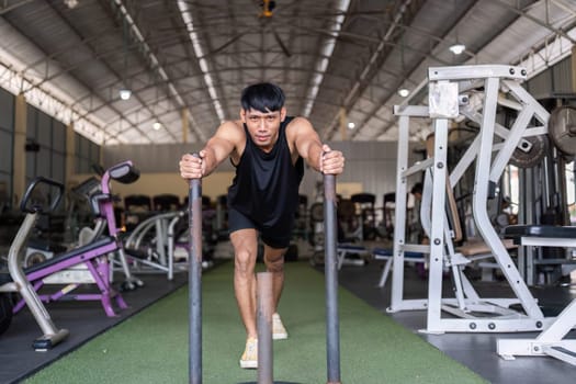 A young man pushes a weighted sled in a gym, demonstrating strength, endurance, and commitment to fitness.