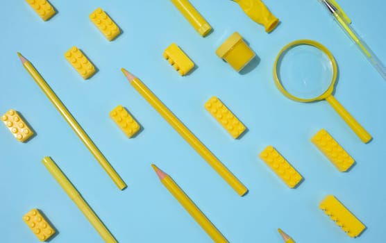 Various yellow objects including pencils, magnifying glass and toy blocks scattered on blue background, top view