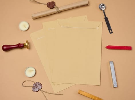 Wax seal kit including wax sticks, spoon, candles, stamp and brown envelopes placed on beige background, top view