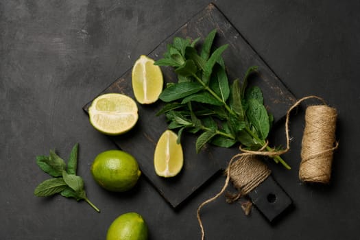 Bunch of fresh green mint and lime wedges on wooden board, top view