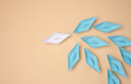 One white origami paper boat leads a group of blue boats on a neutral background
