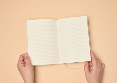 Hands hold a blank open notebook on a neutral background, top view