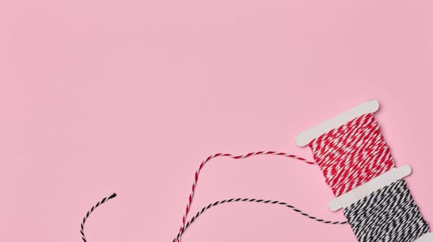 Two spools of red and white and black and white striped twine on a pink background.