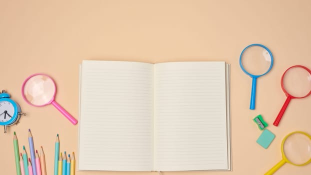 Top view of an open notebook with pastel-colored pencils, green sharpener, and turquoise eraser on a beige background. Flat lay composition of school or office stationery supplie