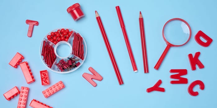 Flat lay of red stationery, learning items letters, magnifying glass, supplies, bricks, toys, and alarm clock on a light blue background. Education, time, and study concept.