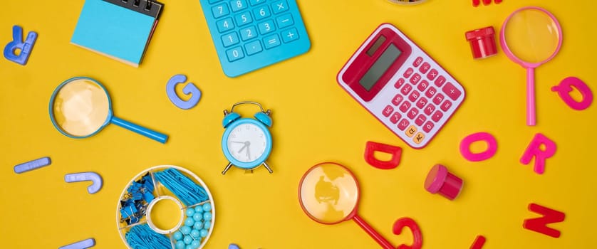 Colorful school supplies, learning items calculators, letters, tools, and stationery scattered on a vibrant yellow background. Education and back to school concept