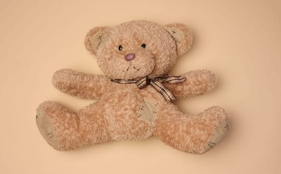 Fluffy brown teddy bear with a ribbon lying on a neutral background, top view