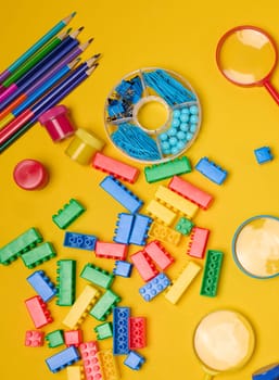 Vibrant collection of colorful school supplies, building bricks, letters, and learning items scattered on a yellow background. Play and education concept.