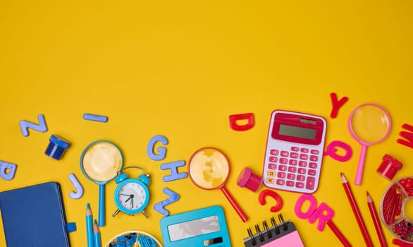 Colorful school supplies, learning items calculators, letters, tools, and stationery scattered on a vibrant yellow background. Education and back to school concept