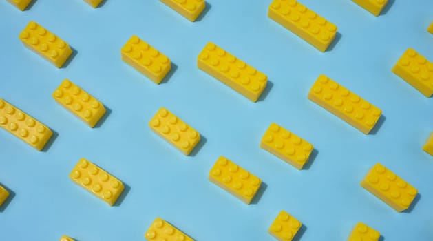 Scattered yellow plastic toy building bricks on a blue background. Play, construction, education or creative concept