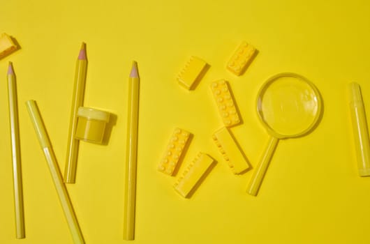 Collection of yellow stationery, building brick, and magnifying glass on a yellow background. Pencil, marker, jar included. Creative or learning concept.