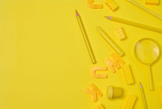 Assortment of yellow stationery and creative items scattered on a yellow background. Pencil, marker, building brick, letter, magnifying glass. Education or art concept