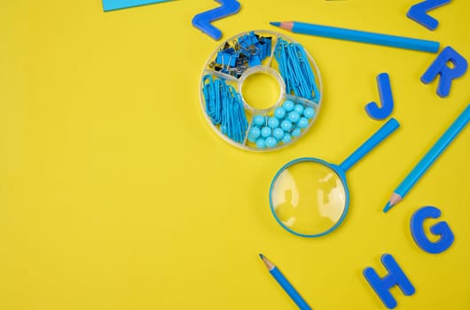 Assortment of blue stationery, letters, paper clips, and supplies scattered on a vibrant yellow background. Education, learning, or art concept.