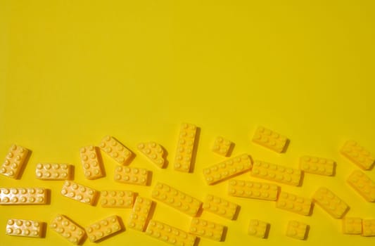 Scattered yellow plastic toy building bricks on a solid yellow background. Play, construction, education or creative concept