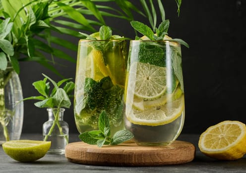 Refreshing detox or summer drink in a glass with lemon, lime, mint, ice, and metal straw. Dark background