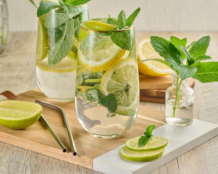 Refreshing citrus and mint drink in glasses with ice, lemon, lime, and mint leaves. Healthy summer beverage