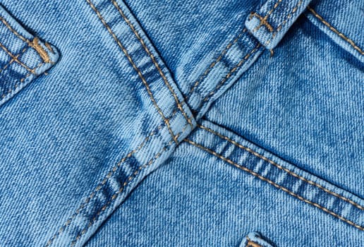 Close-up of blue denim jeans fabric showing reinforced cross-stitching. Detailed view of the seam and textile texture for design and quality themes