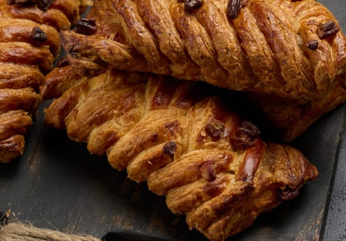 Golden brown maple pecan braid pastries are arranged on a dark, textured surface. Braided dough is flaky and topped with pecans