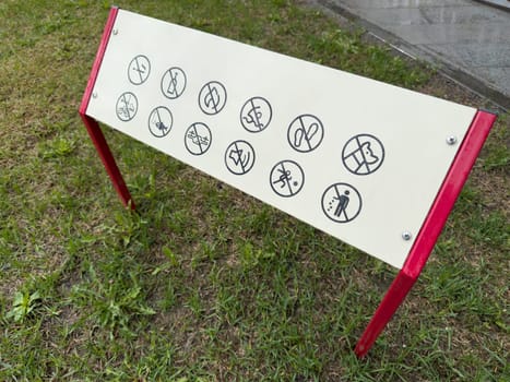 Information board with multiple prohibition icons installed on grass. The sign uses universal symbols to indicate restricted actions in a public area, promoting safety and proper behavior